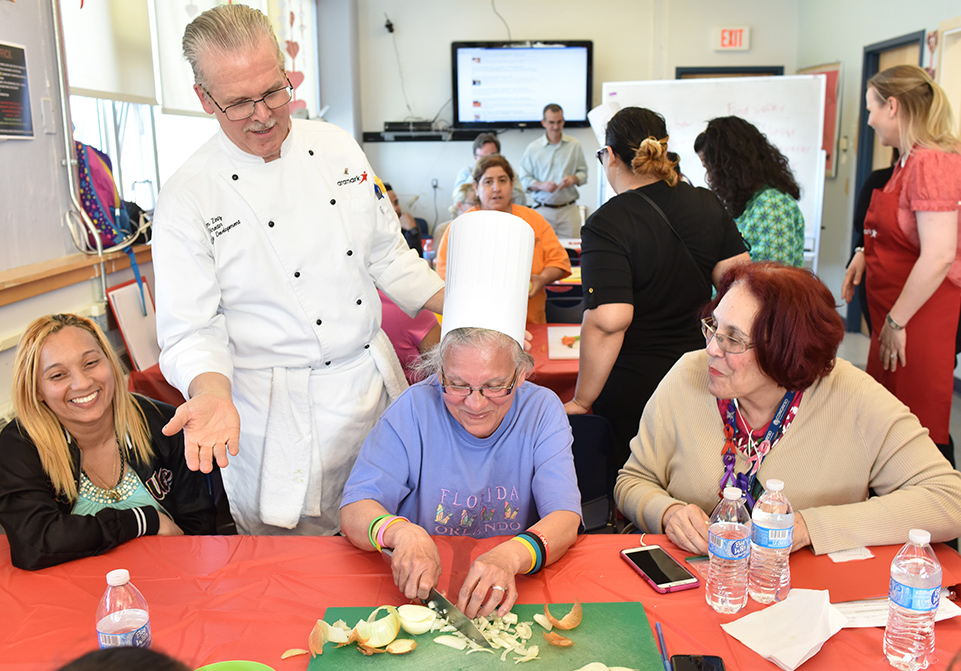 Aramark chef talking to a woman cutting onions in a classroom.